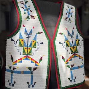 May include: A sleeveless vest featuring intricate white beadwork with geometric patterns in blue, yellow, green, and red. The garment has a deep V-neckline, a red fabric border along the edges, and a green beaded trim outlining the front panels.