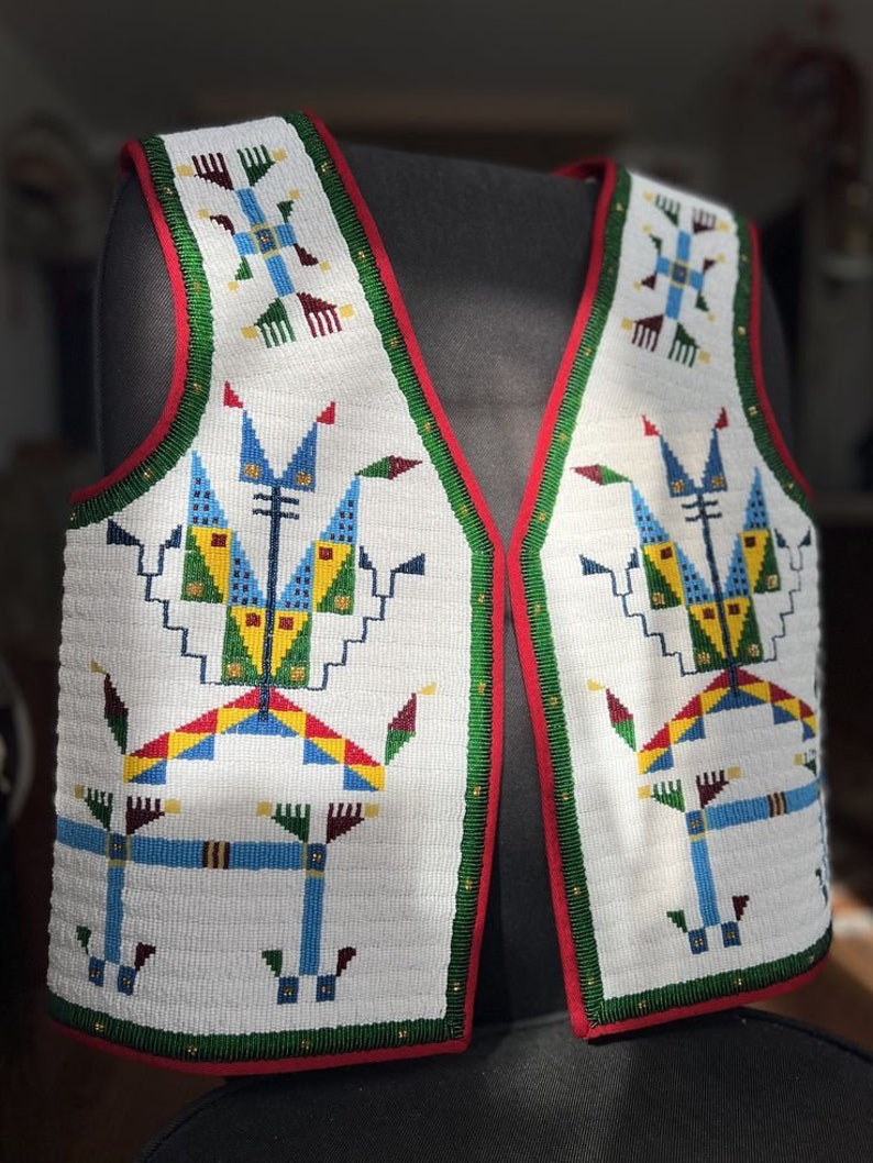 May include: A sleeveless vest featuring intricate white beadwork with geometric patterns in blue, yellow, green, and red. The garment has a deep V-neckline, a red fabric border along the edges, and a green beaded trim outlining the front panels.