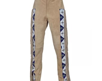 Puede incluir: Pantalón de gamuza marrón claro con detalles de flecos a los lados. Los flecos están decorados con cuentas blancas y detalles azules y verdes.