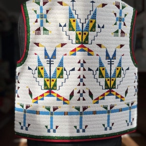May include: A sleeveless vest featuring an intricate white background covered in geometric beadwork patterns. The design incorporates blue, yellow, green, and maroon shapes with a red and green border trim along the armholes and bottom hem.
