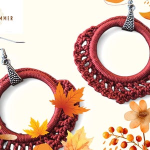 Op de afbeelding: Een paar rode gehaakte oorbellen met zilveren haakjes en een delicaat gehaakt ontwerp. De oorbellen zijn omringd door herfstthema-beelden, waaronder bladeren en bessen.