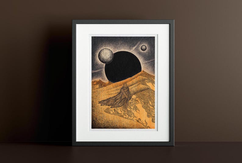 May include: A framed print of a black and white illustration of a desert landscape with a large black orb in the sky and a figure in the foreground. The desert is depicted in shades of gold and brown.