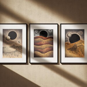 May include: Three framed prints with black frames and white mats. Each print features a black and white illustration of a landscape with a large black circle and smaller white circles in the sky. The landscapes are different in each print.