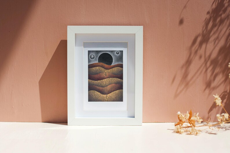 May include: A framed drawing of a landscape with a large black circle in the sky and a series of brown and gold hills.
