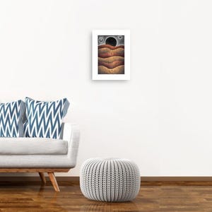 May include: A digital art print of a landscape with a black circle in the sky and brown, orange, and yellow hills. The print is framed in a white frame.