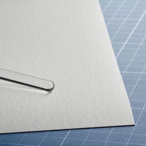 May include: A clear glass stirring rod on a white textured surface.