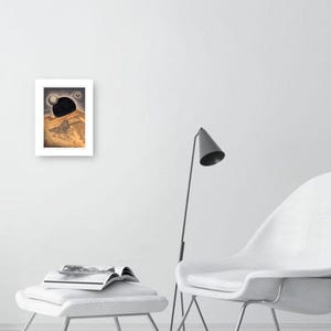 May include: A black and white drawing of a landscape with a large black orb in the sky. The orb is partially obscured by a hill in the foreground. The drawing is framed in a white frame.