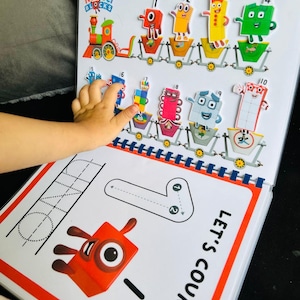 May include: A colorful educational book for children featuring Numberblocks characters. The book includes a train with number blocks, a counting activity, and a tracing activity for the number one. The book has the words "Number Blocks" and "Let's Count" printed on the cover.