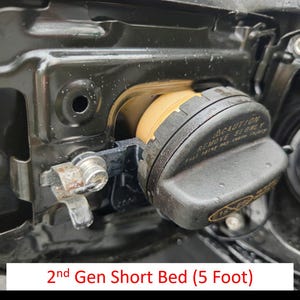 以下が含まれることがあります： 黒い金属製の燃料ドアに、黄色のリングと「CAUTION REMOVE SLOWLY」という文字が書かれた黒い燃料キャップのクローズアップ。燃料ドアの下に「2nd Gen Short Bed (5 Foot)」という文字が見える。