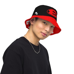 May include: Reversible bucket hat with a black crown and red brim. The black side features a white "B" logo and a red "E" logo. The red side has a white logo. The hat is worn by a person.
