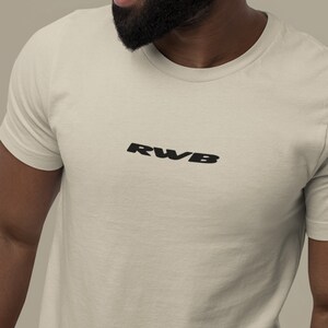 May include: A cream-colored t-shirt with the black letters "RWB" printed across the chest. The shirt has a crew neck and short sleeves. The fabric appears to be a soft, breathable material.