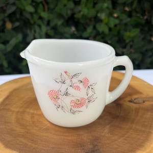 May include: White ceramic creamer with a floral design featuring pink flowers and green leaves.