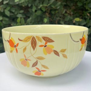 May include: A pale yellow ceramic bowl with a floral design. The bowl features a ribbed exterior and is decorated with orange, yellow, and brown flowers and leaves. The bowl is likely vintage and suitable for serving.