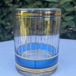 May include: A clear glass tumbler with blue and gold bands. The glass has vertical gold lines and a blue band near the base and top. The word "CLAYERO" is visible on the side of the glass.