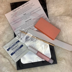 Puede incluir: Un conjunto de suministros para el arte de uñas que incluye una lima de uñas, un empujador de cutículas, un buffer, un frasco de pegamento, un paquete de pestañas adhesivas, una almohadilla de removedor de esmalte de uñas, un empujador de cutículas de madera, una lima de uñas y un frasco de esmalte de uñas rosa. Las instrucciones para aplicar el arte de uñas están impresas en una hoja de papel blanca.