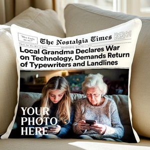 Pode incluir: Uma almofada branca com um design de jornal com uma manchete que diz "Local Grandma Declares War on Technology, Demands Return of Typewriters and Landlines". A imagem mostra duas pessoas, uma menina e uma mulher mais velha, ambas olhando para seus telefones. O texto "YOUR PHOTO HERE" está impresso na almofada.