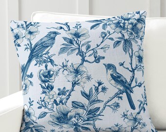 May include: A blue and white throw pillow with a floral pattern and birds. The pillow is on a white couch.