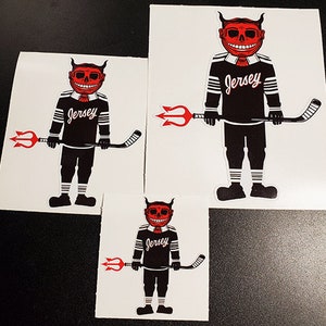 May include: Three different sizes of stickers featuring a red devil character holding a hockey stick. The devil is wearing a black and white jersey with the word "Jersey" printed on it. The stickers are on a white background.