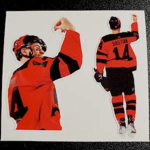 May include: Two stickers featuring a hockey player in a red and black jersey with the name "BASTIAN" and the number "14". One sticker shows the player from the front, the other from the back, both with arms raised in celebration.