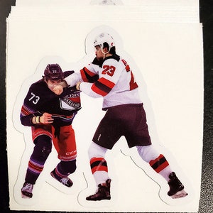 May include: Two hockey players in action, one wearing a white jersey with red and black accents and the number 23, the other wearing a black and blue jersey with the number 73 and the words "New York Rangers".