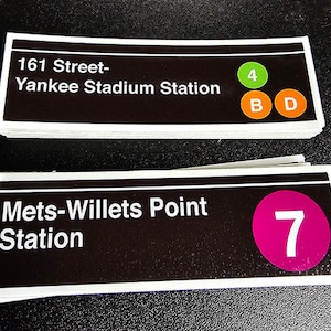 May include: Two black and white subway station signs with white text. The top sign reads "161 Street-Yankee Stadium Station" with a green circle with the number "4" and two orange circles with the letters "B" and "D". The bottom sign reads "Mets-Willets Point Station" with a pink circle with the number "7".