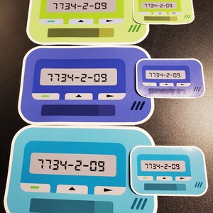 May include: Three different colored pager stickers with the number 7734-2-09 displayed on the screen. The stickers are green, blue, and light blue.