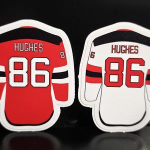 May include: Two hockey jersey-shaped stickers, one red and one white. Both feature the name "HUGHES" above the number "86". The red jersey has black and white accents, while the white jersey has red and black accents. Each has the numbers "6" and "8".