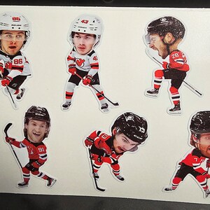 May include: Five hockey player stickers with red, white, and black uniforms. The players are wearing helmets and holding hockey sticks. The stickers are on a white background.