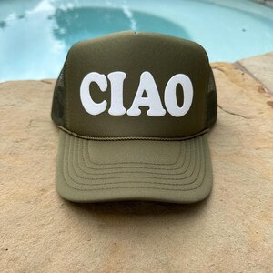 May include: A green trucker hat with a white "CIAO" logo in a retro font. The hat is made of a mesh material and has a curved brim.