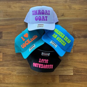 May include: Four trucker hats with mesh backs and foam fronts. The top hat is light purple with purple text reading THROAT GOAT. The left hat is teal with orange text reading I HEART COCKtails. The right is blue with lime text MOISTER THAN AN OYSTER. The bottom is black with pink text RECOVERING SLUT.