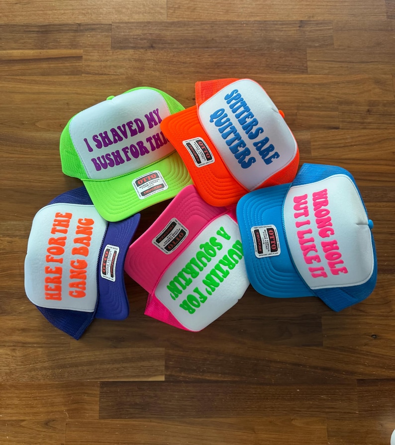 May include: Five foam trucker hats with mesh backs in neon green, orange, pink, blue, and purple. Each hat features a white front panel with printed text: I SHAVED MY BUSH FOR THIS, SPITTERS ARE QUITTERS, HERE FOR THE GANG BANG, SQUIRTIN' FOR A SQUIRTIN', and WRONG HOLE BUT I LIKE IT.
