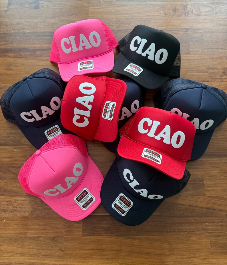 May include: A collection of seven trucker hats with a mesh back. The hats are in various colors, including pink, red, black, and navy blue. Each hat features the word "CIAO" in white, bold letters.