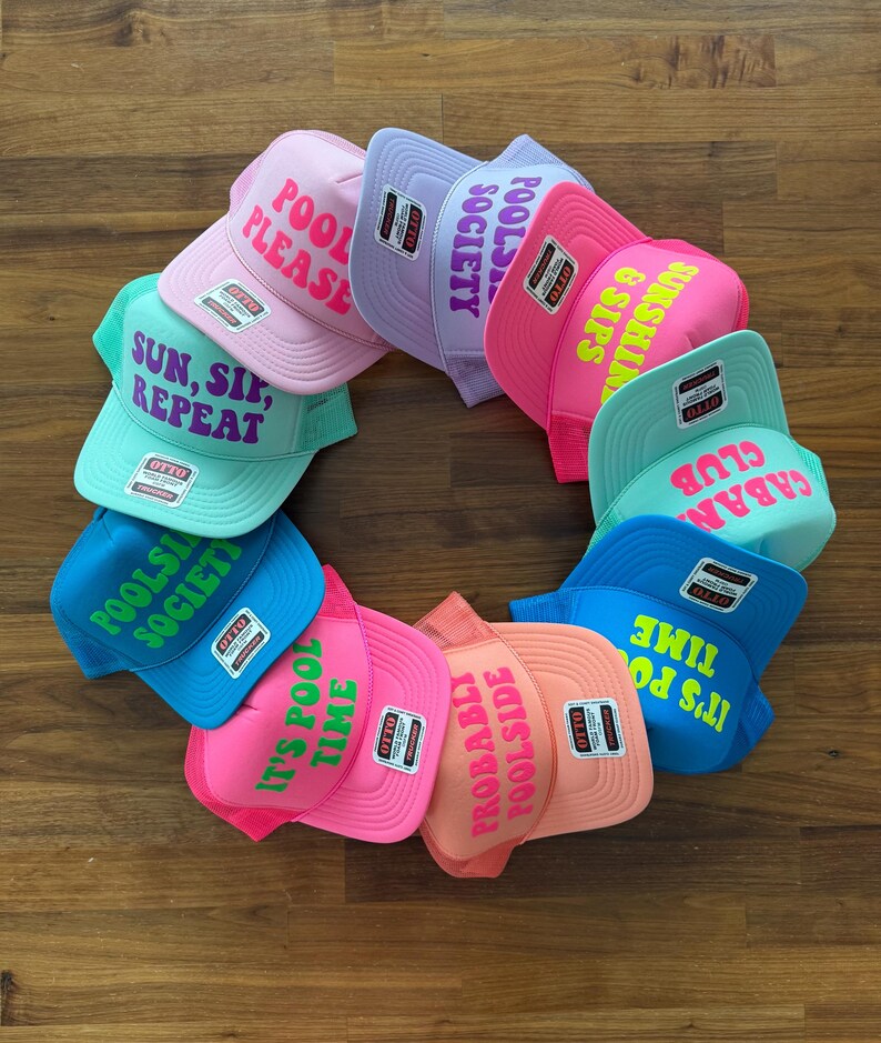 May include: A collection of ten colorful trucker hats arranged in a circle, each featuring unique text such as Pool Please, Poolside Society, Sunshine & Sips, Cabana Club, and It's Pool Time. The hats come in various bright shades including pink, blue, and mint.
