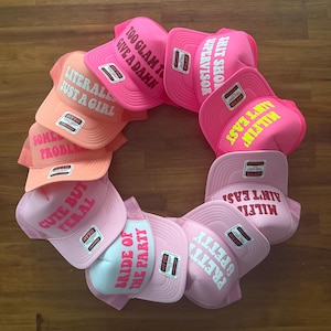 May include: A circular arrangement of ten trucker hats in various shades of pink and orange. Each hat features an OTTO brand sticker and white or yellow text including phrases like LITERALLY JUST A GIRL, TOO GLAM TO GIVE A DAMN, and MILFIN AIN'T EASY.