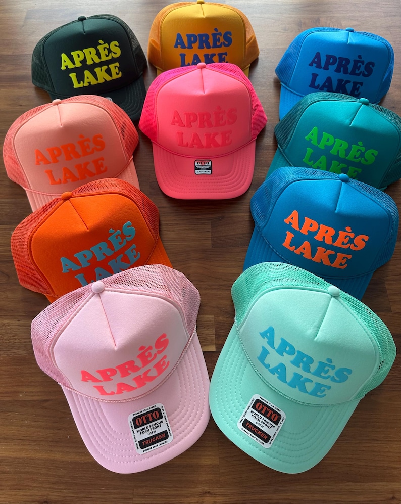 May include: A collection of trucker hats in various colors, including green, yellow, pink, blue, and orange. Each hat features the text "APR&Egrave;S LAKE" in a contrasting color. The hats have a mesh back and a curved brim.