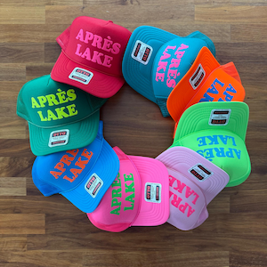 May include: A collection of ten colorful trucker hats arranged in a circle, each featuring the text APR&Egrave;S LAKE in bold lettering. The hats come in various vibrant colors including red, teal, orange, green, blue, pink, and light purple.