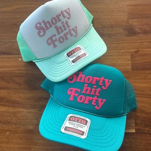 May include: Two trucker hats with the text "Shorty hit Forty" in pink script. One hat is light blue with a light green mesh, the other is teal with a dark green mesh. Both have an "OTTO" tag.