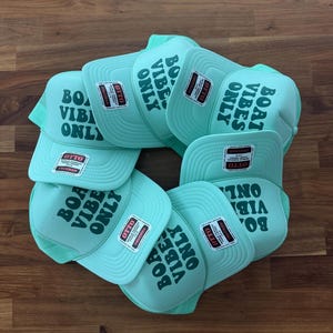 May include: A collection of light mint green trucker hats featuring a mesh back and a foam front panel. Each hat displays the dark green text "BOAT VIBES ONLY" printed on the front and includes an attached Otto brand tag on the brim.