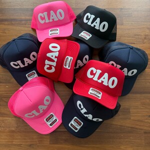 May include: A collection of six trucker hats in various colors, including pink, red, black, and navy blue. Each hat features the word "CIAO" in a large, white, retro font.