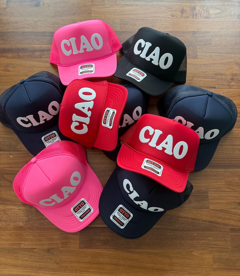 May include: A collection of six trucker hats in various colors, including pink, red, black, and navy blue. Each hat features the word "CIAO" in a large, white, retro font.