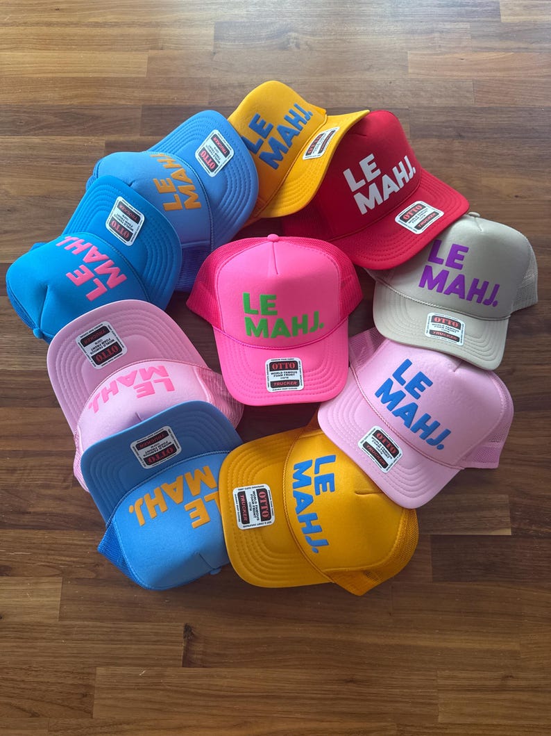May include: A collection of ten trucker hats in various colors including yellow, red, light blue, bright blue, pink, and beige. Each hat features the text LE MAHJ. printed on the front panel in a contrasting color and includes an Otto brand label.