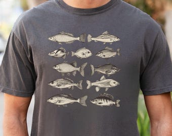 Puede incluir: Una camiseta gris oscuro con una ilustración vintage de varios peces impresos en la parte delantera. Los peces son en blanco y negro y están dispuestos en una fila.