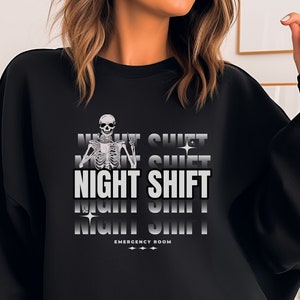 May include: Black sweatshirt with a skeleton graphic and the text "NIGHT SHIFT" repeated in a gradient effect. The text "EMERGENCY ROOM" is also printed on the sweatshirt.