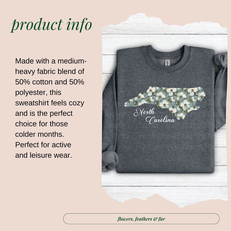 May include: A dark gray sweatshirt featuring a floral North Carolina state outline. The design includes white flowers on a light blue background, with "North Carolina" in script. The sweatshirt is made of a medium-heavy fabric blend.