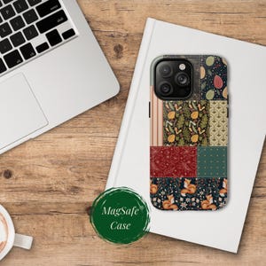May include: A MagSafe phone case with a patchwork design. The case features various patterns, including stripes, floral, and fox motifs, in a palette of red, green, and navy blue. The case is resting on a white book next to a laptop.
