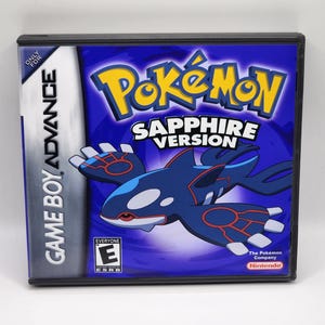 以下が含まれることがあります： 青いゲームボーイアドバンスのゲームカートリッジと、青と赤のポケモンサファイアバージョンゲームケース。ケースには、白腹の青と赤のポケモンの漫画画像が描かれています。