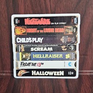 May include: A stack of VHS tapes featuring classic horror movies, including "Nightmare on Elm Street", "Night of the Living Dead", "Child's Play", "Scream", "Hellraiser", "Friday the 13th", and "Halloween".