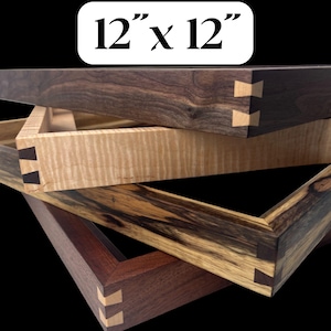May include: Three wooden picture frames, each with a different wood grain and color, are stacked on top of each other. The frames are all 12 inches by 12 inches and have a mitered corner joint. The top frame is dark brown, the middle frame is light brown, and the bottom frame is a dark brown with a lighter wood grain.