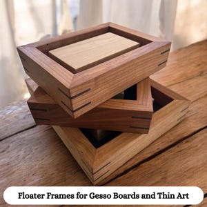 May include: Three wooden picture frames stacked on top of each other. The frames are made of natural wood with a light brown finish. The frames have a simple design with a slightly raised lip around the edge. The frames are designed to float artwork, such as gesso boards and thin art, off the surface of the frame.
