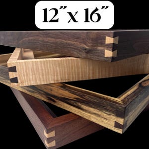 May include: A stack of four rectangular wooden trays measuring 12 inches by 16 inches. Each tray features visible dovetail joinery with contrasting light and dark wood keys. The wood grains vary in color from dark brown to light tan and striped patterns.